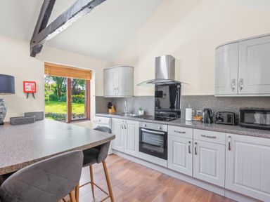 A kitchen with grey cabinets and appliances and a breakfast bar with stools at The Stables in St Neot