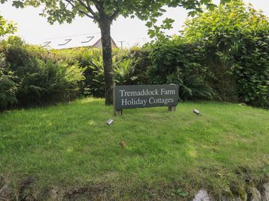 A sign on grass under a tree with bushes in the background at Tremaddock Farm Holiday Cottages