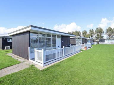 A group of modern single storey holiday chalets with white fences and green lawns at 104 The Laurels in Chapel St Leonards