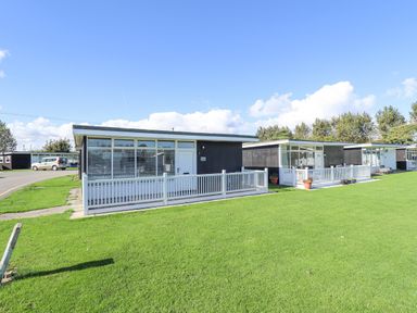 Small black and white holiday chalets with fenced patios on a grassy lawn at 104 The Laurels in Chapel St Leonards