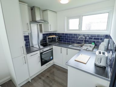 A kitchen with white cabinets blue tiled backsplash oven microwave sink and toaster at 104 The Laurels in Chapel St Leonards
