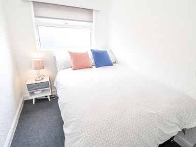 A bedroom with a bed with two cushions and a bedside table with a lamp at 104 The Laurels in Chapel St Leonards