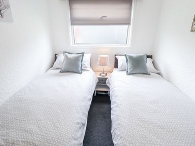 A bedroom with two single beds separated by a nightstand with a lamp at 104 The Laurels in Chapel St Leonards