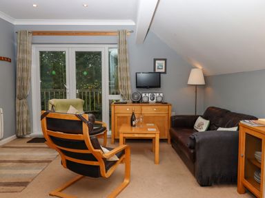 A sitting room with leather armchairs a wooden table a floor lamp and a TV on a wooden cabinet at 5 Lakeview Rise Highampton near Hatherleigh