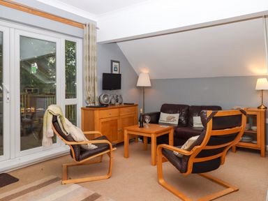 A living room with two wooden framed chairs a leather sofa wooden tables a sideboard and glass doors at 5 Lakeview Rise Highampton near Hatherleigh