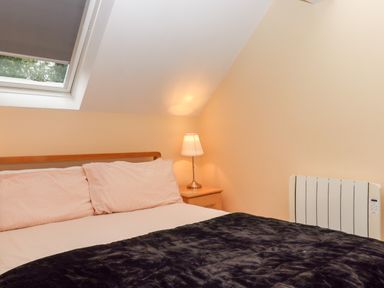 A bedroom with a bed a bedside table with a lamp and a window at 5 Lakeview Rise in Highampton near Hatherleigh