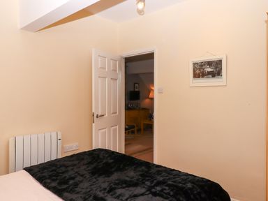 A bedroom with a bed covered in a black blanket and an open door showing a living room at 5 Lakeview Rise Highampton near Hatherleigh