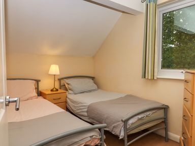 A bedroom with two single beds a wooden nightstand with a lamp a window and a wooden chest of drawers at 5 Lakeview Rise Highampton near Hatherleigh