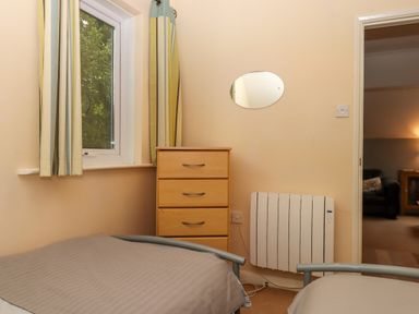 A bedroom with two single beds a wooden chest of drawers a window with curtains and a wall-mounted radiator at 5 Lakeview Rise Highampton near Hatherleigh