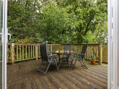 A wooden deck with a black outdoor table and four chairs surrounded by trees at 5 Lakeview Rise Highampton near Hatherleigh