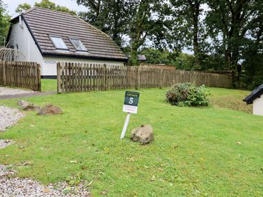 A grassy yard with a reserved parking sign and a fenced white cottage with skylights at 5 Lakeview Rise Highampton near Hatherleigh
