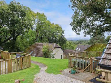 An outdoor area with wooden decks and railings surrounded by trees and rooftops at 5 Lakeview Rise in Highampton near Hatherleigh