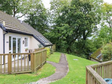 Exterior view of a house with a wooden deck and railing next to a curved path and green lawn at 5 Lakeview Rise Highampton near Hatherleigh