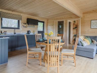 A wooden dining table with chairs in a kitchen area with blue cabinets and a gray sofa with pillows at Foxglove in Higher Wambrook near Chard