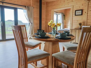 A dining area with wooden chairs and a round table set with dishes and a vase of yellow flowers at Foxglove in Higher Wambrook near Chard
