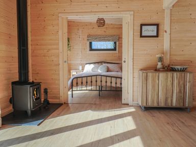 A wooden room with a black wood stove on the left and a wooden cabinet on the right with a bedroom visible through a doorway at Foxglove in Higher Wambrook near Chard