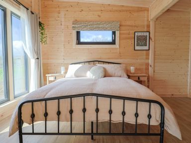 A bedroom with a metal bed frame a window nightstands and wooden walls at Foxglove in Higher Wambrook near Chard