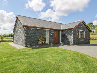 A stone house with wooden door and windows surrounded by lawn at Bwthyn Clyd in Llanddaniel Fab