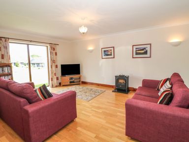 A living room with two red sofas and a television near a sliding glass door at Bwthyn Clyd in Llanddaniel Fab