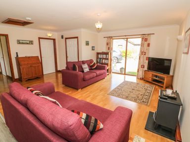 A living room with red sofas a wooden cabinet a television and a bookcase at Bwthyn Clyd in Llanddaniel Fab