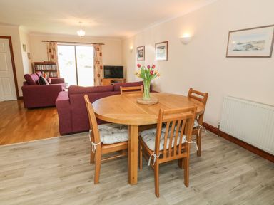 A dining area with a wooden table and chairs next to a living room with sofas and a television at Bwthyn Clyd in Llanddaniel Fab