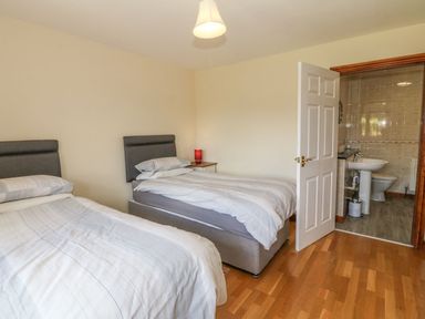A bedroom with two single beds a bedside table with a lamp and an open door leading to a bathroom at Bwthyn Clyd in Llanddaniel Fab