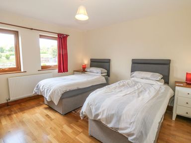 A bedroom with two single beds bedside tables with lamps and two windows at Bwthyn Clyd in Llanddaniel Fab