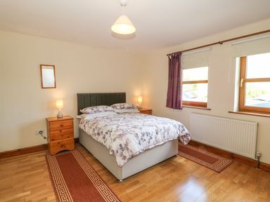 A bedroom with a double bed between two wooden nightstands with lamps and two windows with curtains at Bwthyn Clyd in Llanddaniel Fab
