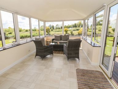 A sunroom with wicker chairs a sofa and a glass table overlooking a garden at Bwthyn Clyd in Llanddaniel Fab