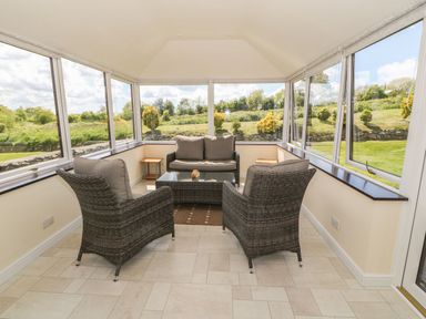 A sunroom with wicker chairs and a loveseat around a glass coffee table at Bwthyn Clyd in Llanddaniel Fab