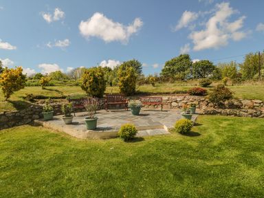 A garden patio area with benches and potted plants surrounded by grass and stone walls at Bwthyn Clyd in Llanddaniel Fab