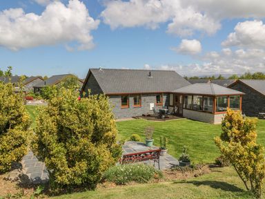 A stone house with a tiled roof and a lawn with bushes and a bench at Bwthyn Clyd in Llanddaniel Fab