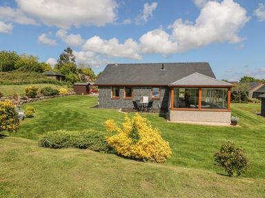 A house with a garden and outdoor seating on a lawn at Bwthyn Clyd in Llanddaniel Fab