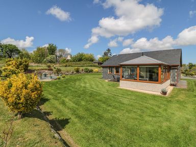 A garden with lawn shrubs pots and a building with large windows at Bwthyn Clyd in Llanddaniel Fab