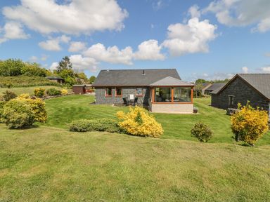 A stone house with a sunroom and patio furniture in a grassy garden with shrubs at Bwthyn Clyd in Llanddaniel Fab