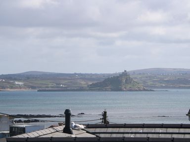 A coastal view with a castle on a hill across the water and rooftops in the foreground at Karenza in Penzance