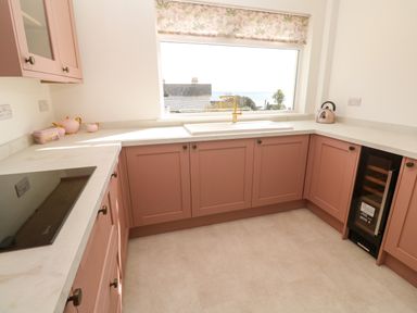 A kitchen with pink cabinets white countertops a window above the sink and a built in wine cooler at Karenza in Penzance