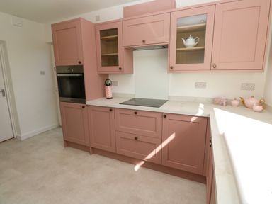 A kitchen with pink cabinets a black oven a bottle on the counter and a pink tea set at Karenza in Penzance