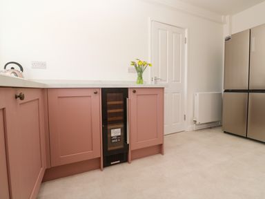 A kitchen with pink cabinets a wine cooler a stainless steel refrigerator and a vase with yellow flowers on the counter at Karenza in Penzance