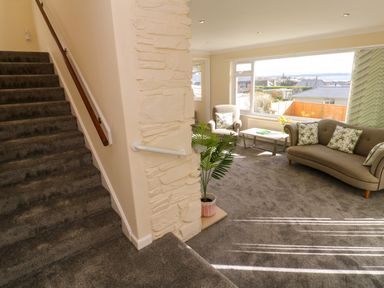A living room with a sofa an armchair a coffee table and a plant next to carpeted stairs at Karenza in Penzance