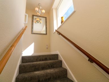 A staircase with carpeted steps handrails on both sides a window with a vase and a mirror on the wall at Karenza in Penzance