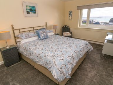 A bedroom with a bed with patterned blue bedding two bedside tables with lamps a chair and a window with a view at Karenza in Penzance