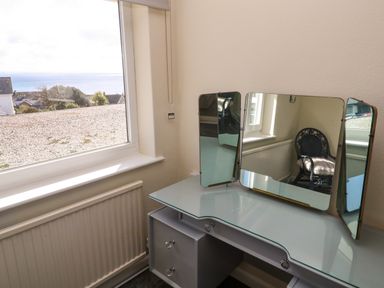 A dressing table with a tri-fold mirror and a window showing a view of rooftops and the sea at Karenza in Penzance