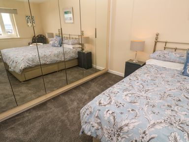 A bedroom with a double bed next to mirrored wardrobes and bedside tables with lamps at Karenza in Penzance