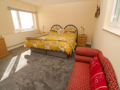 A bedroom with a yellow floral bedspread two wooden bedside tables a red patterned sofa and a window at Karenza in Penzance