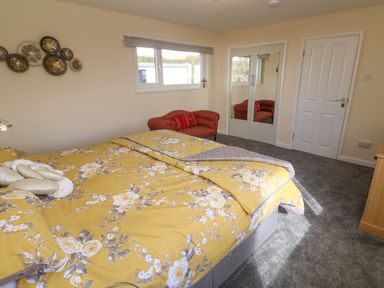A bedroom with a double bed with yellow floral bedding a red chair window and mirrored closet doors at Karenza in Penzance