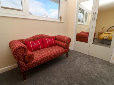 A red patterned sofa with red cushions under a window next to a white mirrored wardrobe in a bedroom at Karenza in Penzance