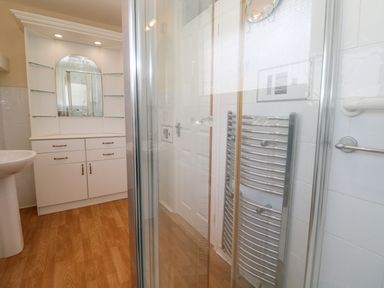 A bathroom with a white sink pedestal cabinet with mirror and glass shelves wood floor and a chrome towel radiator at Karenza in Penzance