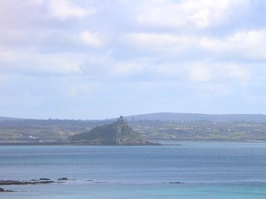 A coastal landscape with a rocky island and a castle surrounded by water at Karenza in Penzance