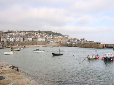 A harbor with boats floating on water and houses on a hill at Karenza in Penzance